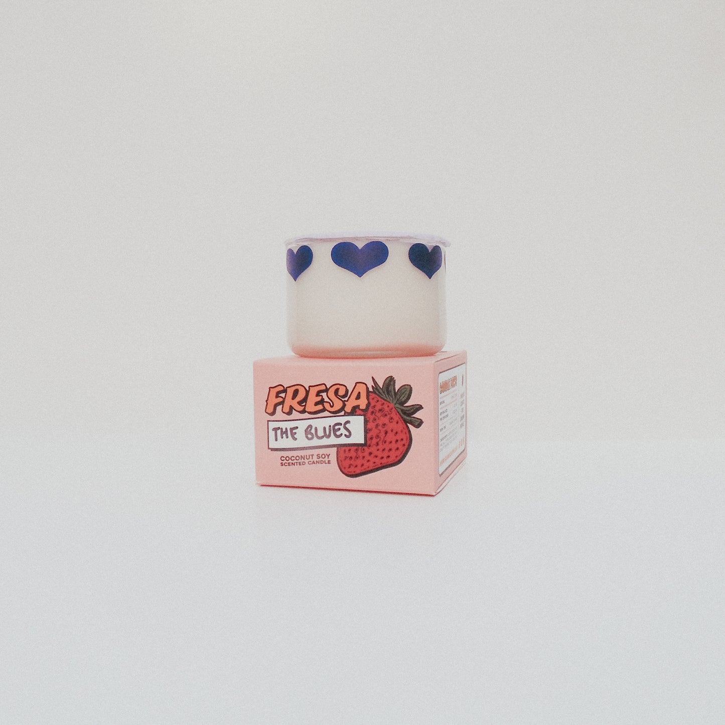 Candle with 'Fresa' branding and strawberry design on a white background