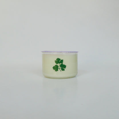 Candle in a glass container with a green leaf design on a light gray background