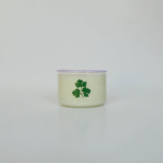 Candle in a glass container with a green leaf design on a light gray background