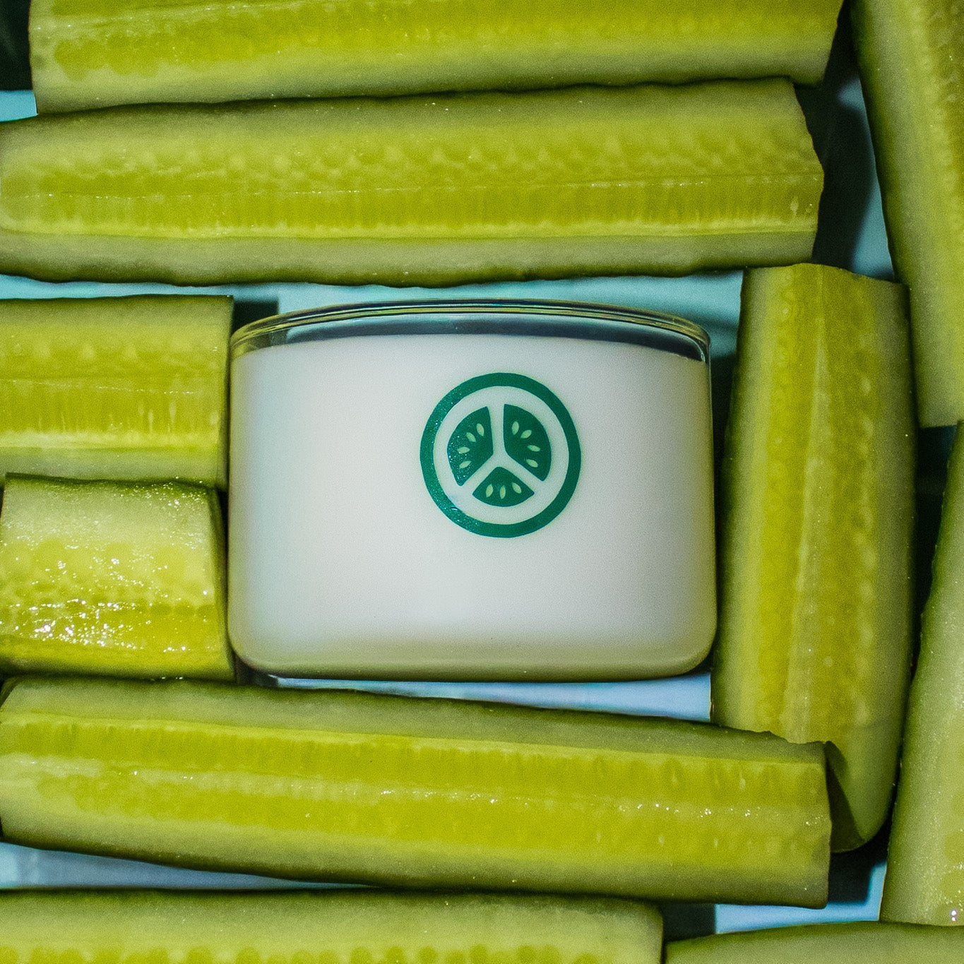 Cucumbers arranged around a small container with a green cucumber logo on a blue background