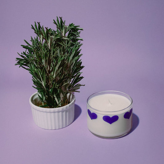 Small potted plant next to a candle with purple hearts on a purple background