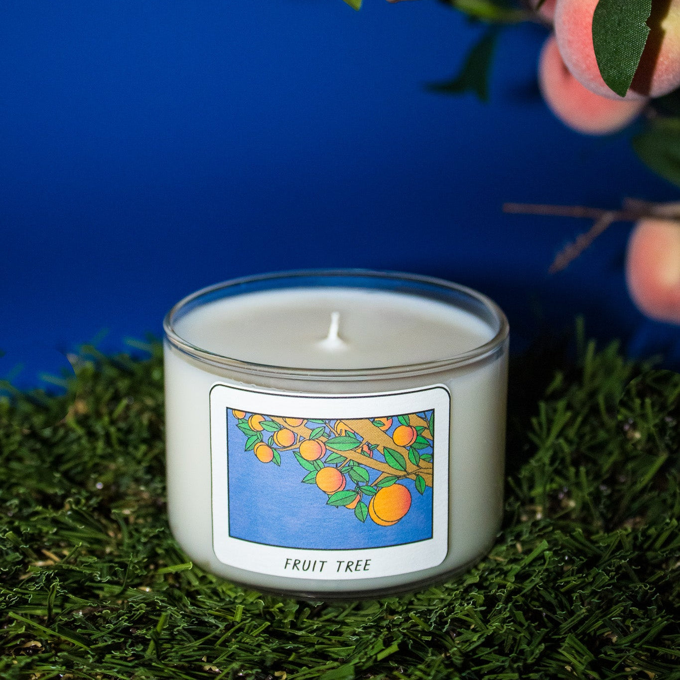 Candle labeled 'Fruit Tree' with peach branches in the background