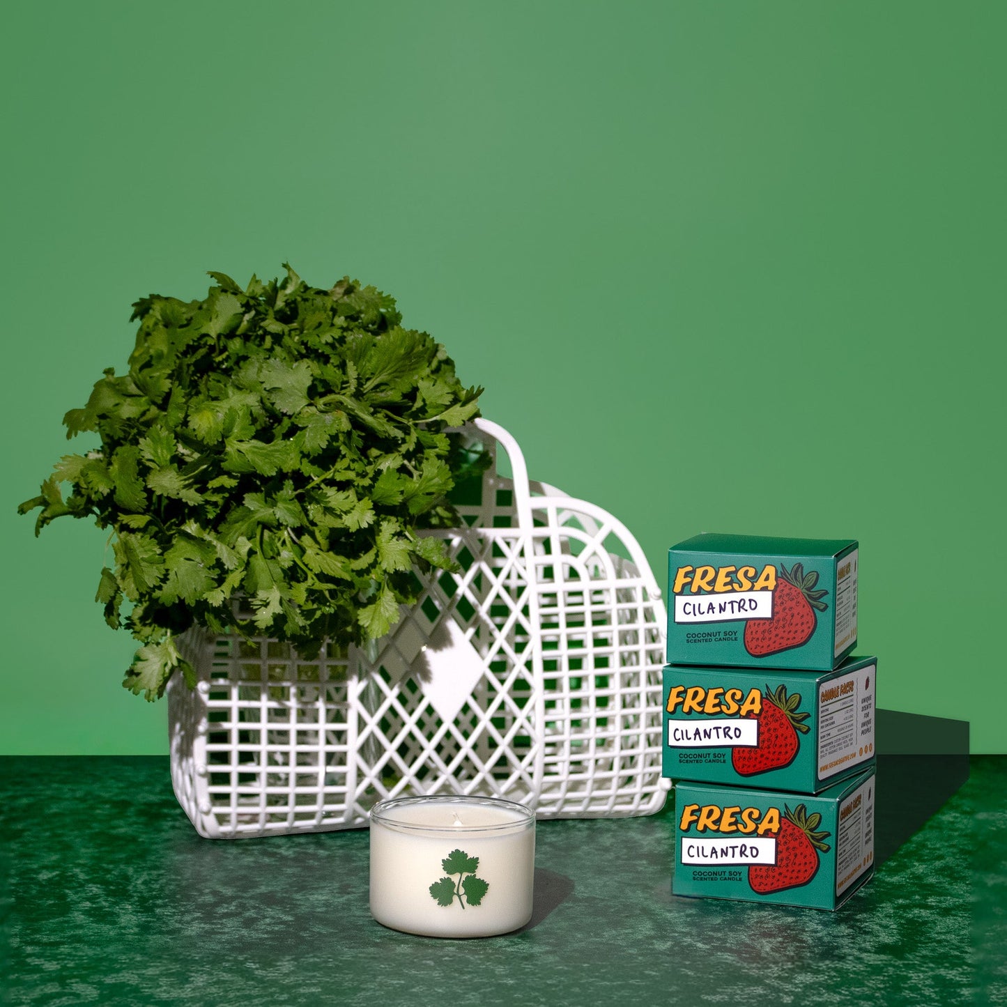 Stack of 'Fresa' boxes with a basket of greens and a candle on a green surface.