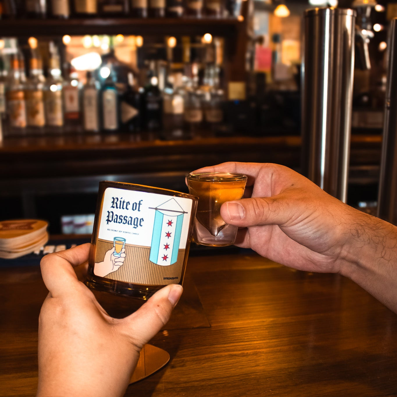 Two hands holding a shot glass and a bottle labeled 'Rite of Passage' in a bar setting.